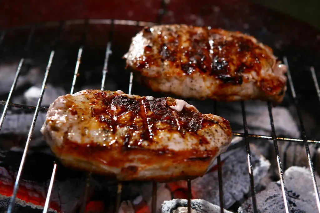 Marinated chicken breasts grilling with lime halves and a bowl of marinade nearby.