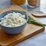 A simple bowl of cottage cheese placed on a rustic wooden cutting board, showcasing its creamy texture.