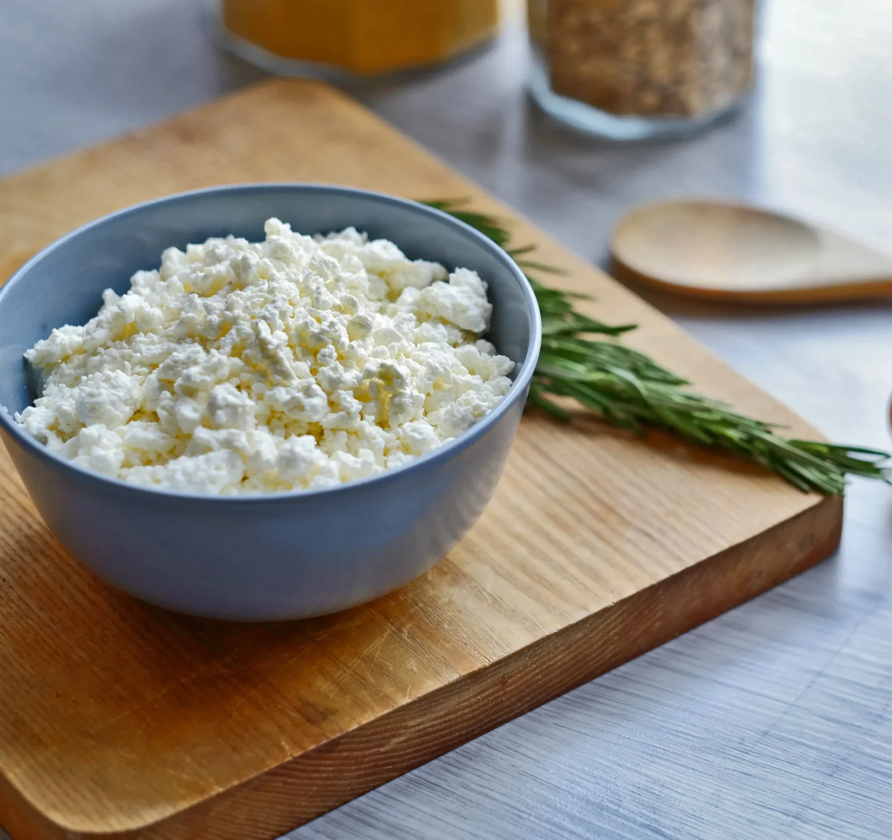 A simple bowl of cottage cheese placed on a rustic wooden cutting board, showcasing its creamy texture.