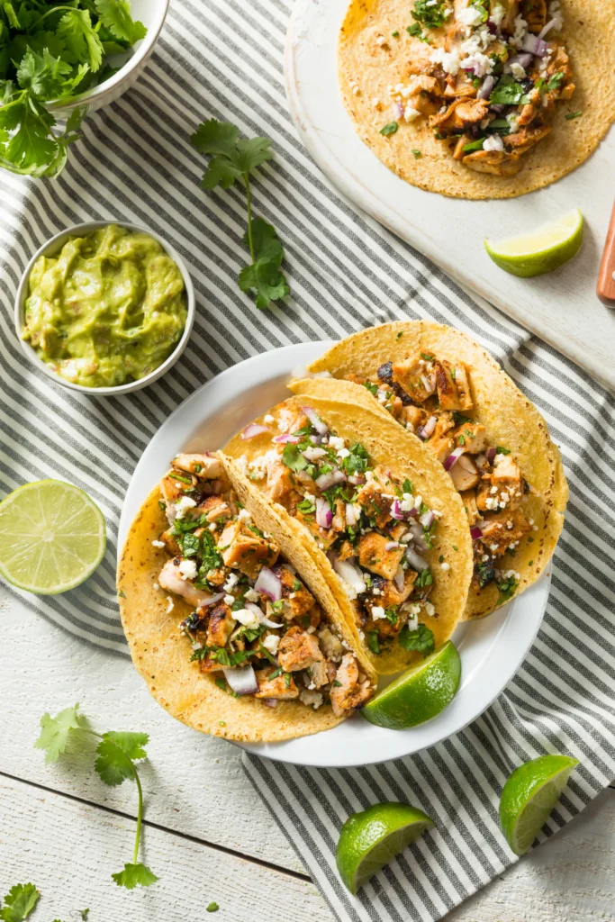 Chicken street tacos with fresh toppings on a rustic table, accompanied by salsa and guacamole.